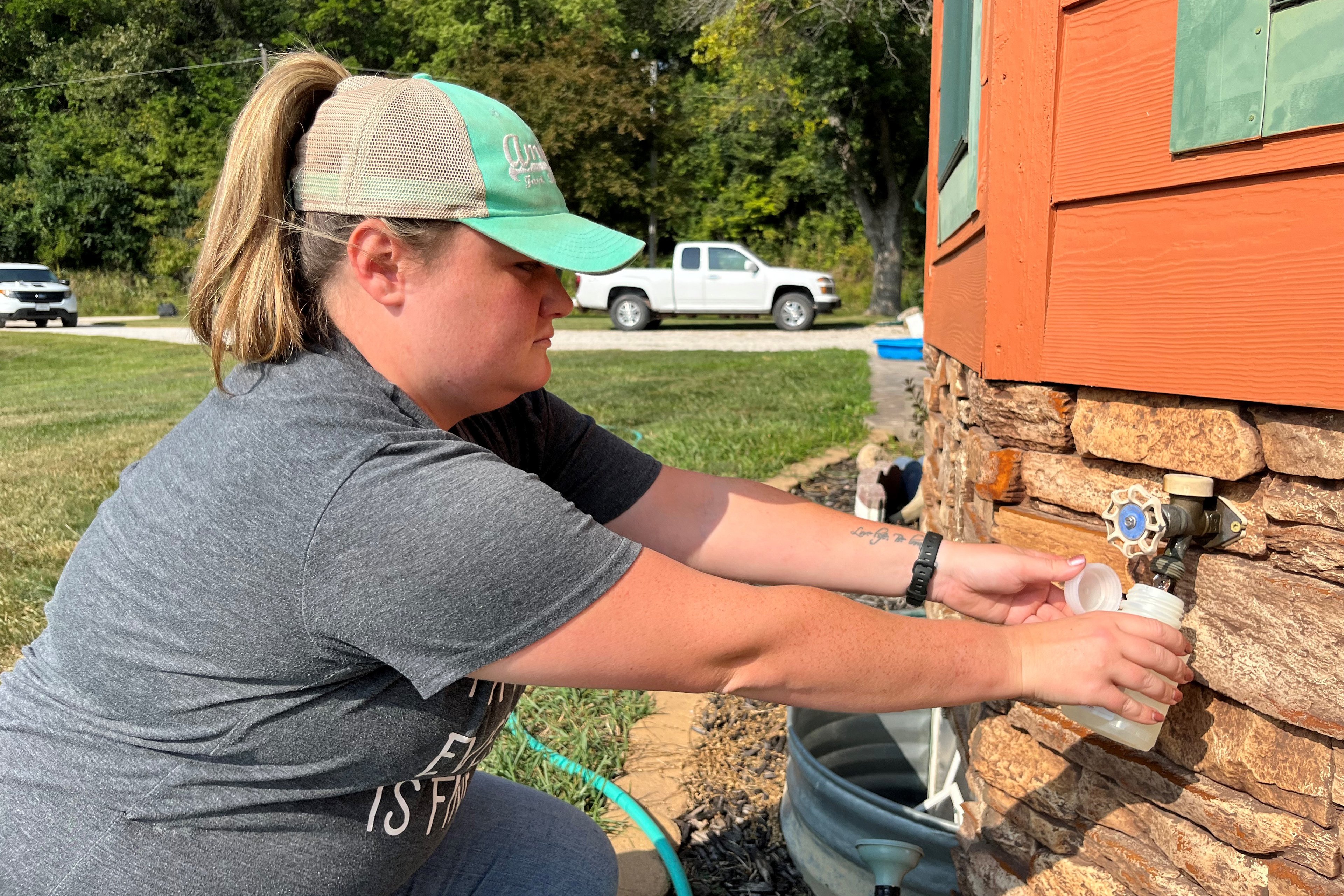 A person filling a white bottle with water from an outdoor spigot.
