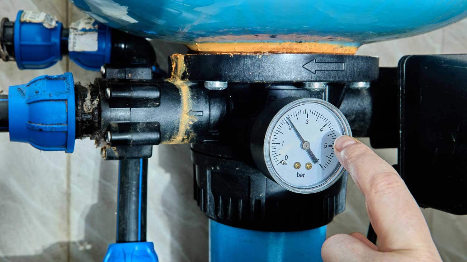 A hand is pointing at a pressure gauge on a pipe system, which measures around 4.7 bar.