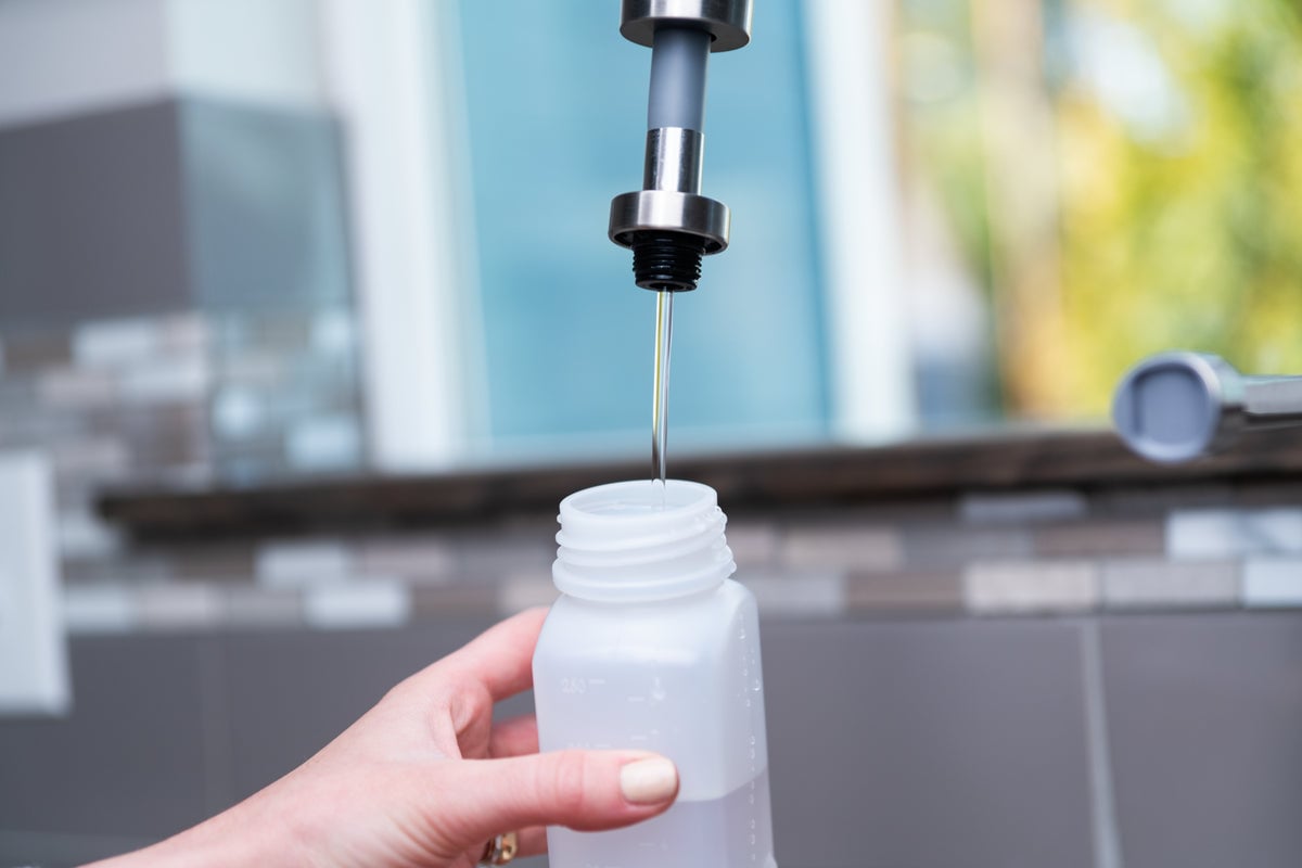 A close-up of a person's hand holding an open water bottle under a faucet as it is being filled with liquid.
