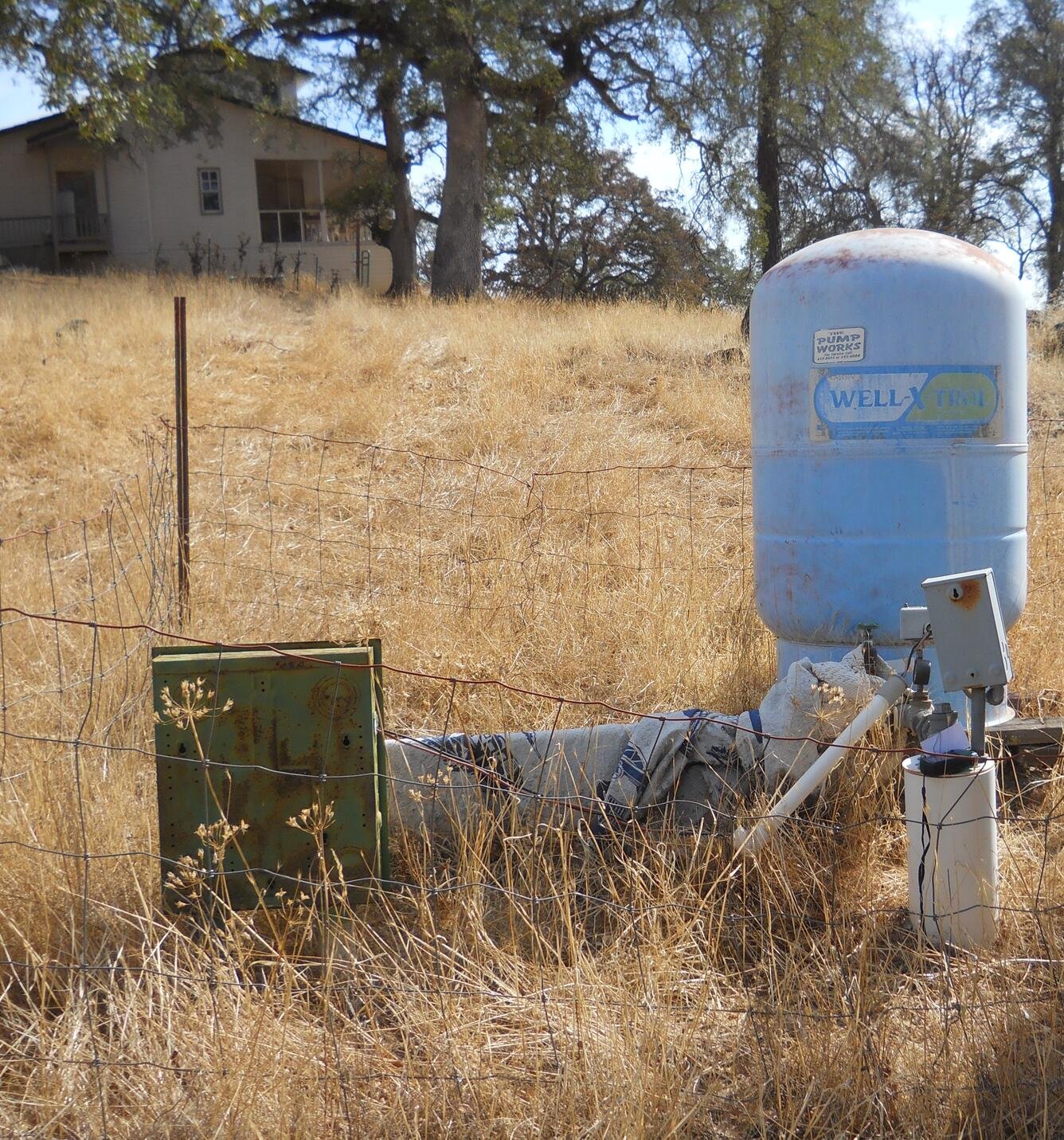 A blue water pressure tank and adjacent equipment in a dry grass field